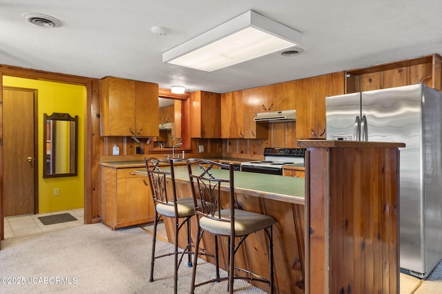 24671 Gardner Rd, Versailles, MO 65084 - kitchen with electric stove, under cabinet range hood, stainless steel refrigerator with ice dispenser, and brown cabinetry
