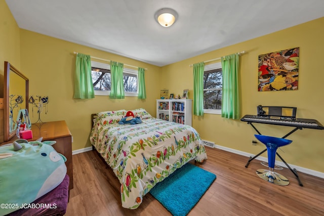 bedroom featuring visible vents, multiple windows, baseboards, and wood finished floors