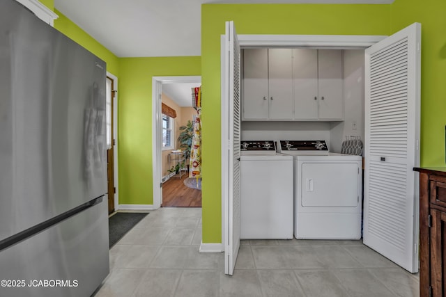 clothes washing area with washing machine and dryer, light tile patterned floors, cabinet space, and baseboards