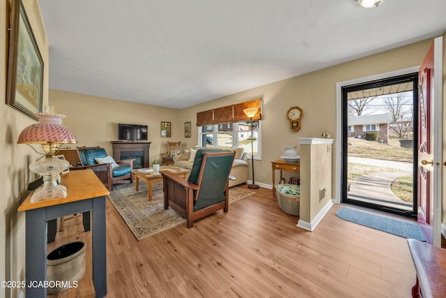 living area featuring light wood-type flooring, baseboards, and a glass covered fireplace