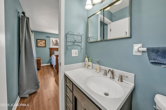 bathroom with vanity, toilet, wood finished floors, and baseboards