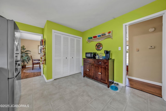 bedroom with a closet, light tile patterned floors, freestanding refrigerator, and baseboards