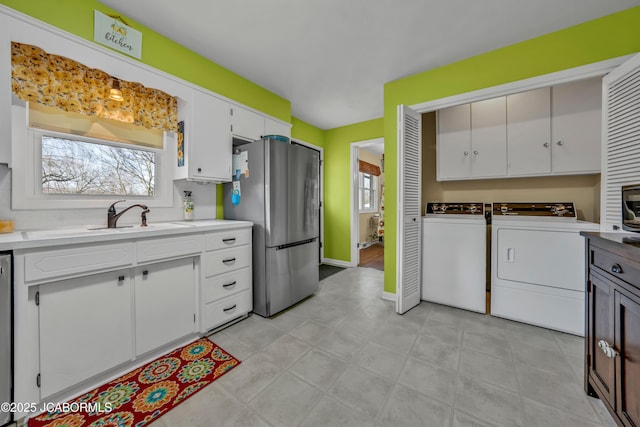 kitchen featuring washer and dryer, white cabinetry, freestanding refrigerator, and a sink