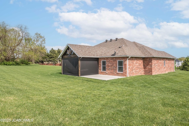 rear view of property featuring a lawn, brick siding, roof with shingles, and a patio