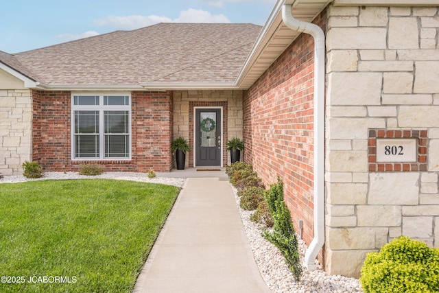 doorway to property with a lawn, brick siding, and a shingled roof