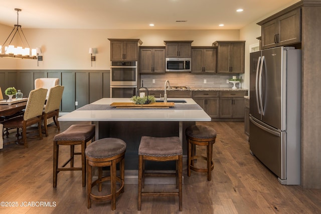 kitchen featuring a wainscoted wall, a sink, an inviting chandelier, light countertops, and appliances with stainless steel finishes
