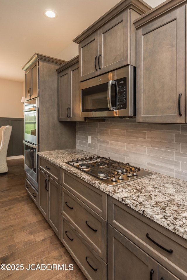 kitchen with dark wood-type flooring, backsplash, appliances with stainless steel finishes, and dark brown cabinetry