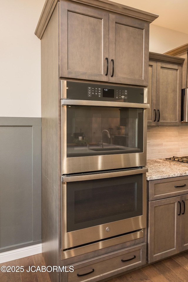 interior details featuring decorative backsplash, light stone counters, stainless steel appliances, and dark wood-type flooring