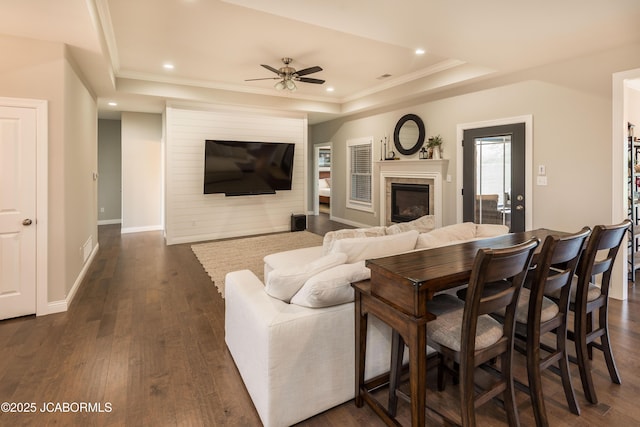 living room with a ceiling fan, a glass covered fireplace, dark wood-type flooring, and a raised ceiling