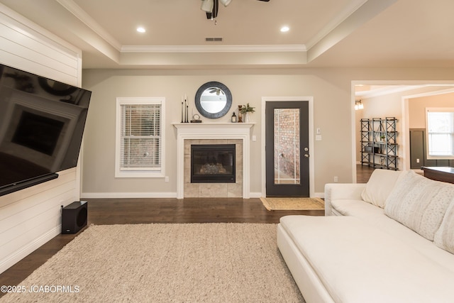 living area with a raised ceiling, crown molding, dark wood-style floors, and a tiled fireplace