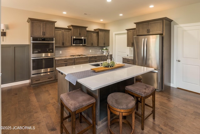 kitchen with dark wood finished floors, appliances with stainless steel finishes, a sink, and a kitchen island with sink