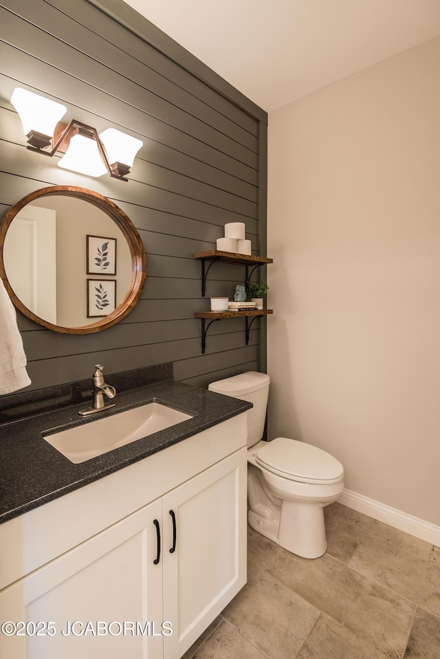 bathroom with wooden walls, baseboards, toilet, and vanity