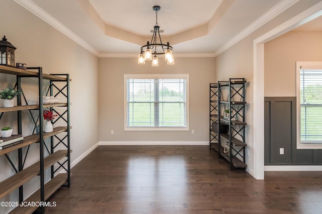 unfurnished dining area featuring dark wood finished floors, an inviting chandelier, baseboards, and a raised ceiling