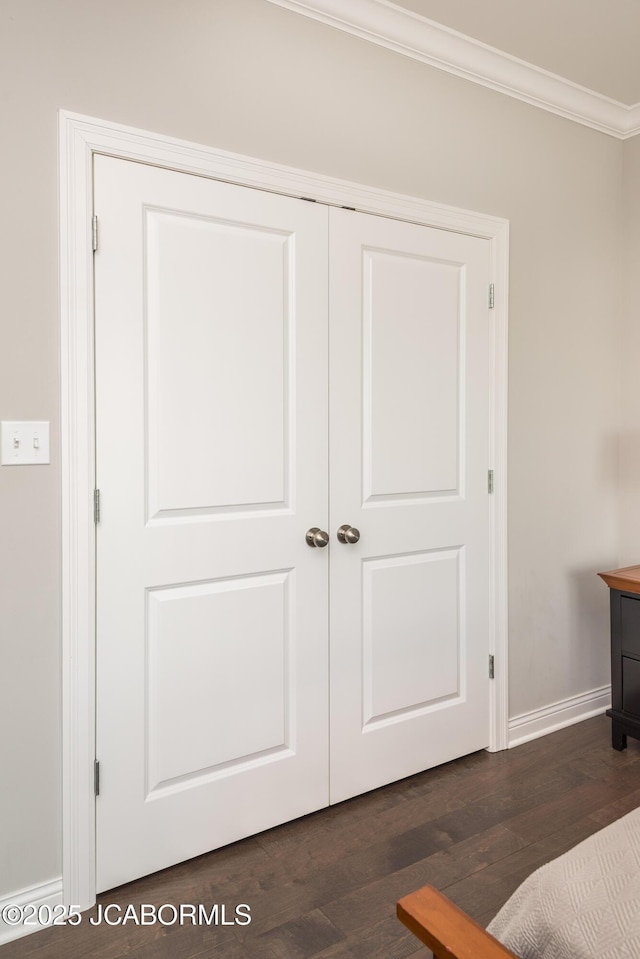 bedroom with dark wood-type flooring, a closet, baseboards, and ornamental molding