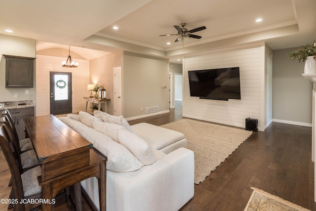 living room featuring dark wood-style floors, visible vents, recessed lighting, ceiling fan with notable chandelier, and a raised ceiling