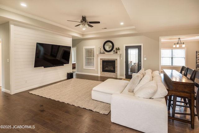 living area featuring a tile fireplace, a raised ceiling, dark wood-type flooring, baseboards, and ceiling fan