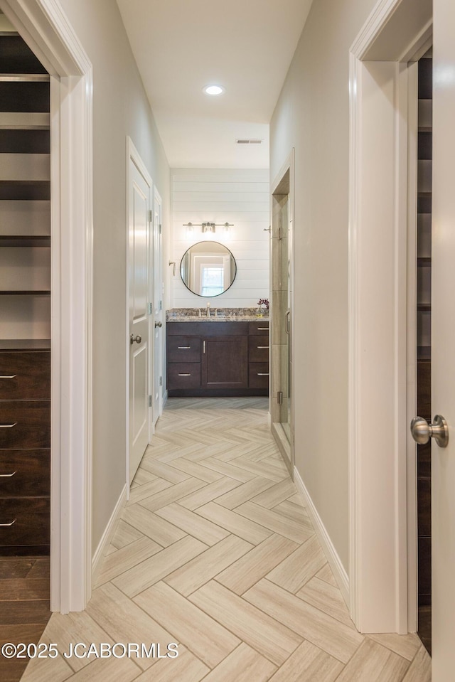 corridor featuring recessed lighting, visible vents, baseboards, and a sink