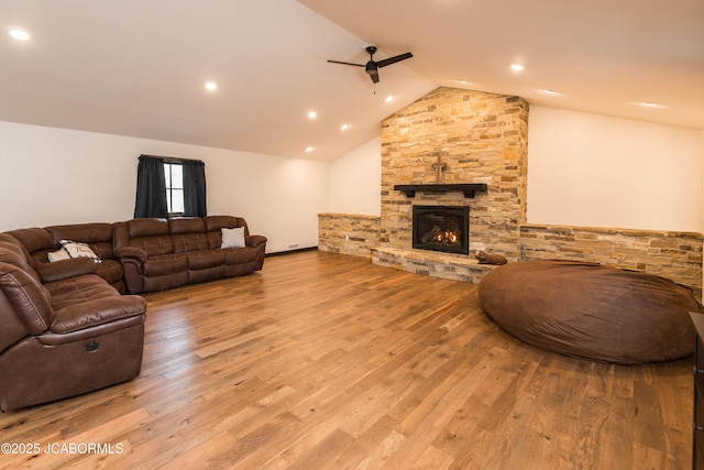 living room featuring a stone fireplace, vaulted ceiling, a ceiling fan, and wood finished floors