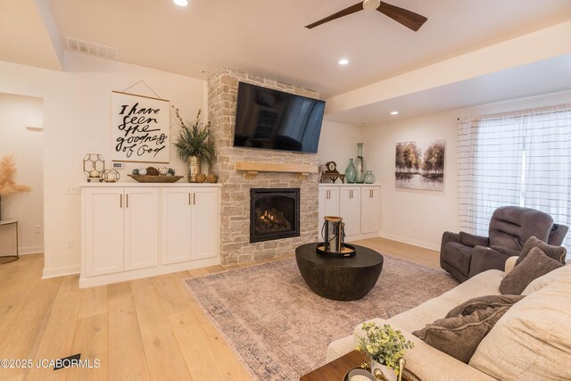 living room with a fireplace, light wood-style flooring, visible vents, and a ceiling fan