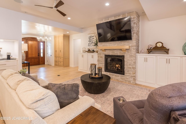 living area with ceiling fan with notable chandelier, a stone fireplace, light wood finished floors, and recessed lighting