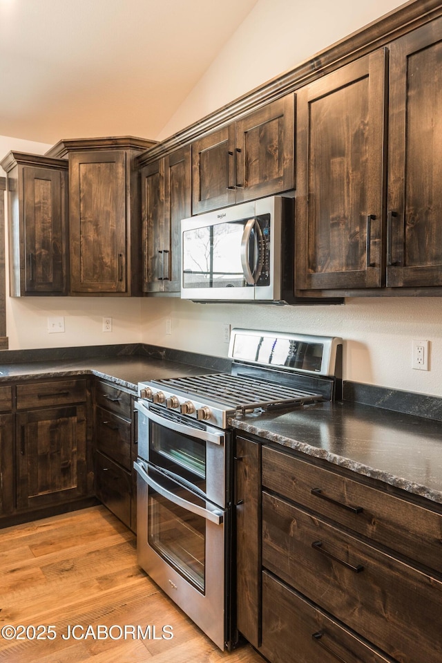 kitchen featuring vaulted ceiling, dark countertops, dark brown cabinetry, light wood-style flooring, and appliances with stainless steel finishes