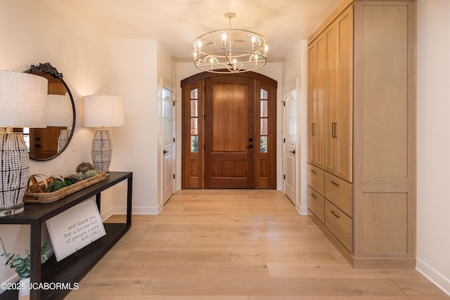 foyer with light wood finished floors, an inviting chandelier, baseboards, and arched walkways