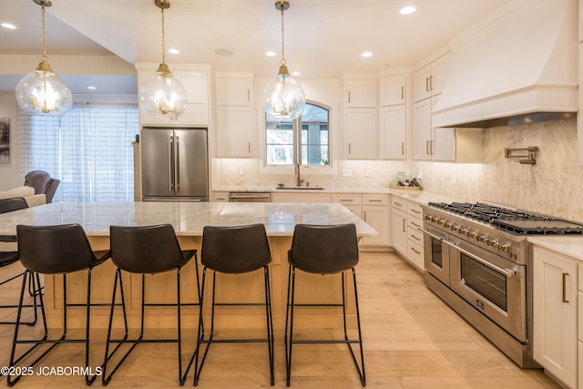 kitchen with a sink, premium appliances, custom range hood, white cabinets, and light stone countertops