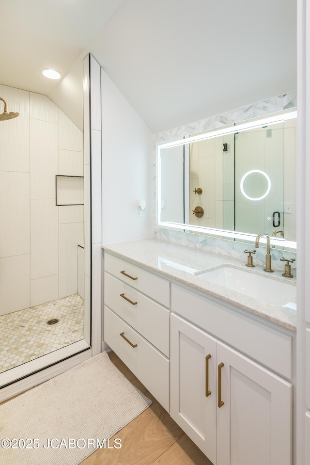 full bath with vaulted ceiling, a sink, double vanity, and tiled shower