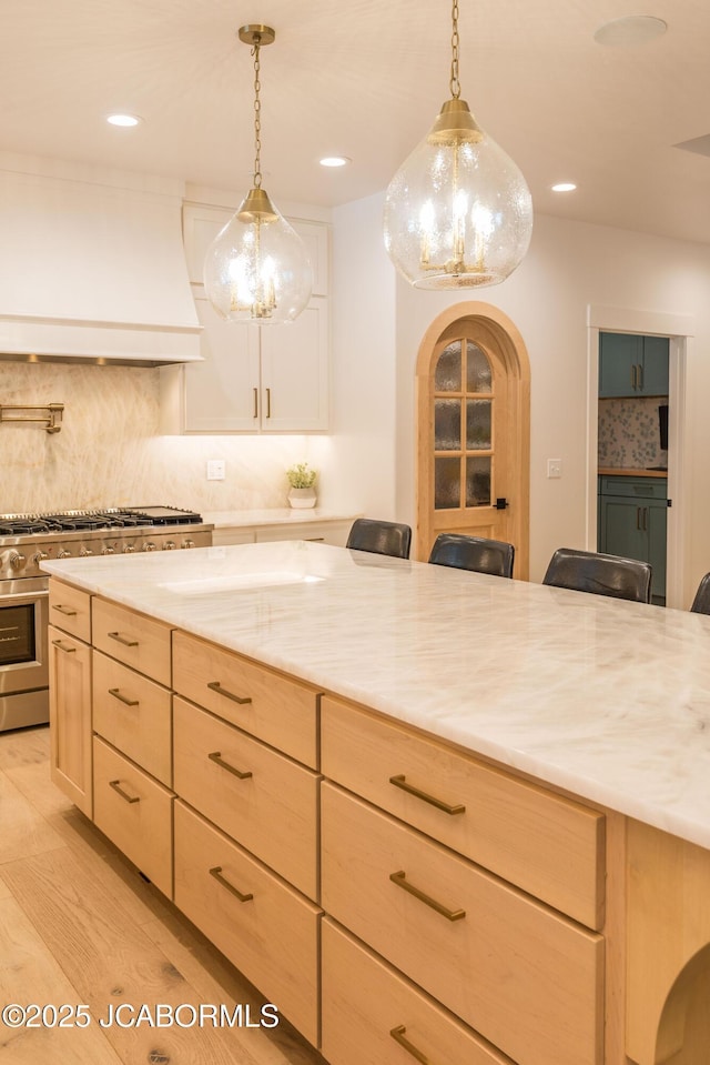 kitchen featuring light brown cabinetry, high end stainless steel range oven, decorative light fixtures, tasteful backsplash, and custom range hood