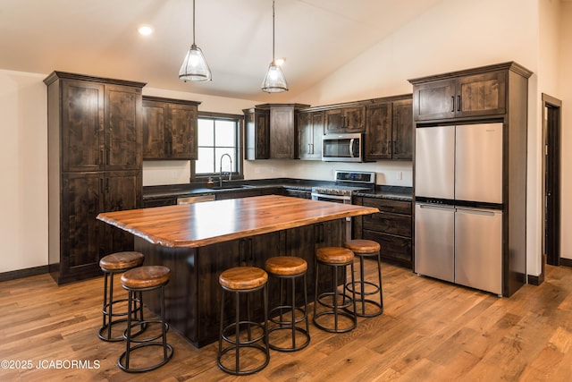 kitchen featuring a sink, dark brown cabinetry, appliances with stainless steel finishes, butcher block counters, and a breakfast bar area