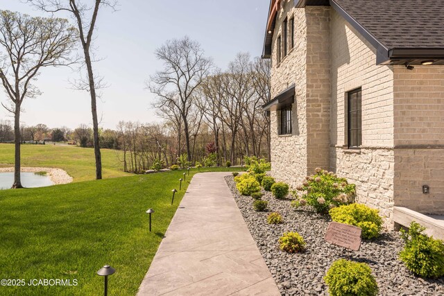 view of side of property with brick siding, a yard, roof with shingles, and stone siding