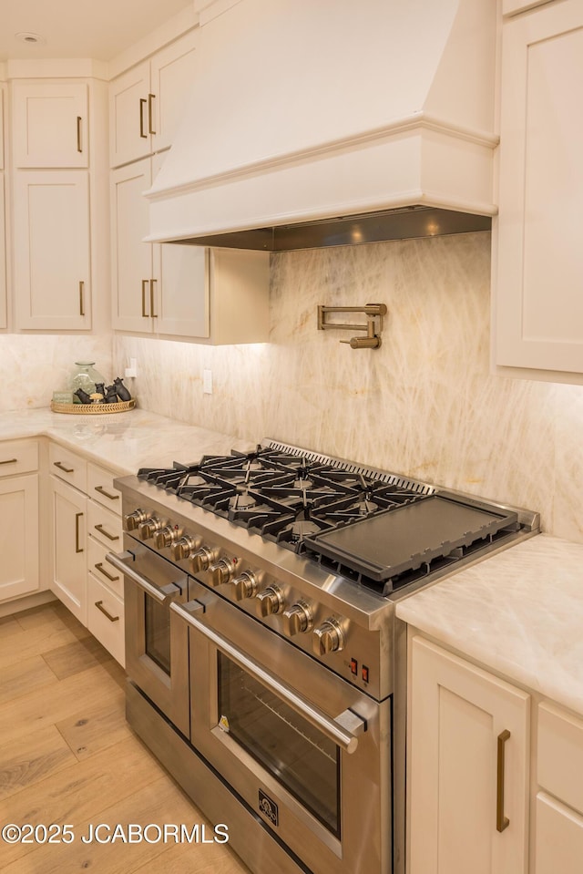 kitchen with white cabinets, double oven range, decorative backsplash, light wood-style flooring, and custom exhaust hood