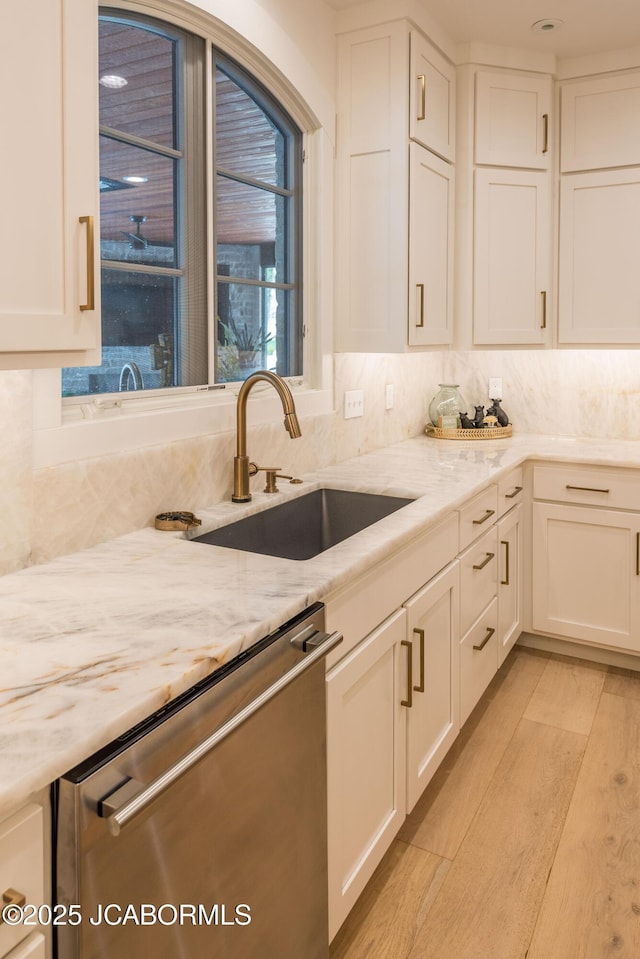 kitchen with dishwasher, white cabinets, light stone countertops, and a sink