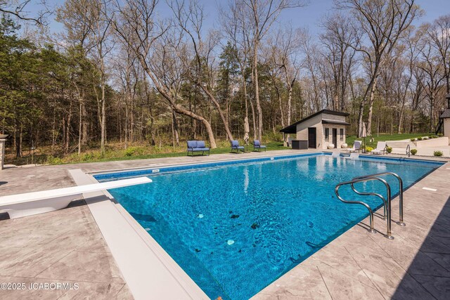 outdoor pool featuring a storage structure, an outdoor structure, a diving board, and a patio