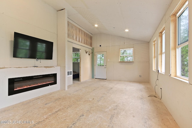 unfurnished living room featuring lofted ceiling, a glass covered fireplace, visible vents, and a wealth of natural light
