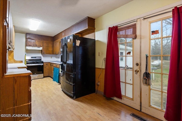 kitchen with black fridge, light hardwood / wood-style flooring, gas range, decorative backsplash, and a textured ceiling