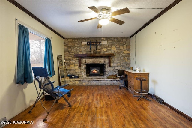 living area with hardwood / wood-style flooring, a stone fireplace, ceiling fan, and ornamental molding