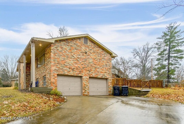 view of side of property with a garage, brick siding, concrete driveway, and fence