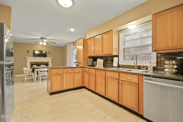 kitchen featuring ceiling fan, decorative backsplash, a peninsula, stainless steel appliances, and a sink