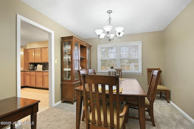 dining room featuring baseboards, light colored carpet, and a chandelier