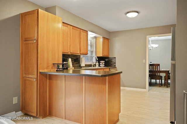 kitchen featuring baseboards, a peninsula, freestanding refrigerator, a sink, and tasteful backsplash