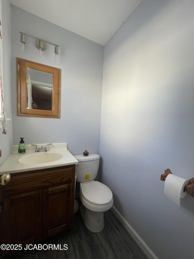 half bathroom with a textured ceiling, toilet, wood finished floors, vanity, and baseboards