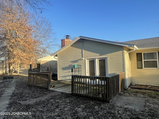 back of house with a deck, a chimney, and fence