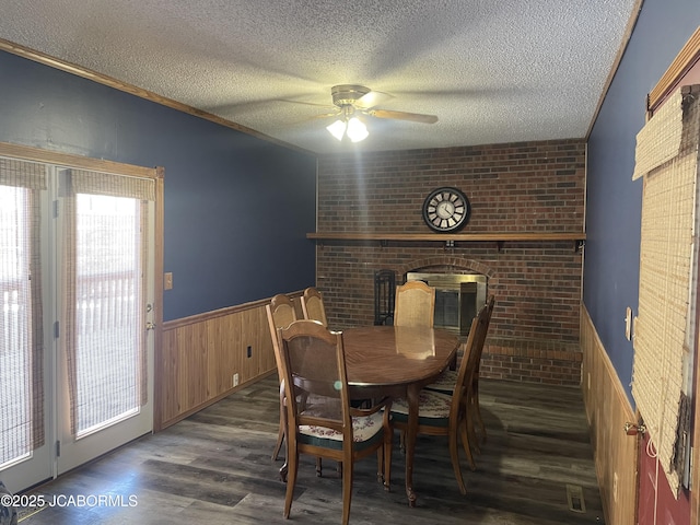 dining room with ceiling fan, dark wood-type flooring, wood walls, and a textured ceiling