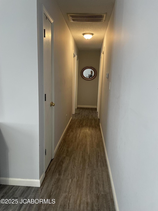 hall featuring a textured ceiling, dark wood-style floors, visible vents, and baseboards