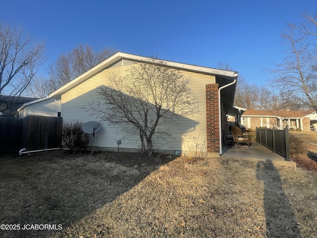 view of side of home featuring brick siding, fence, and a patio