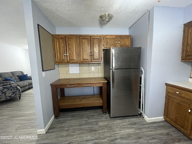 kitchen with brown cabinets, dark wood-type flooring, backsplash, and freestanding refrigerator