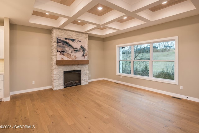 unfurnished living room featuring coffered ceiling, a stone fireplace, light hardwood / wood-style floors, and beamed ceiling