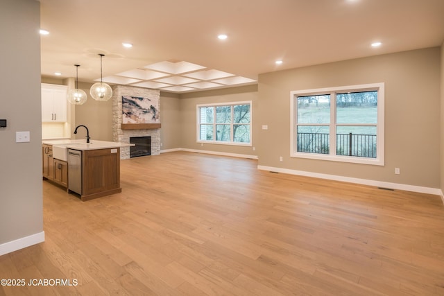 kitchen featuring pendant lighting, dishwasher, a fireplace, an island with sink, and white cabinets