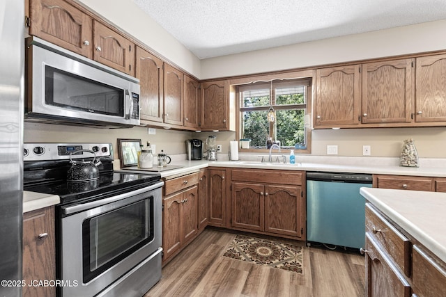 kitchen with light wood-type flooring, a sink, a textured ceiling, appliances with stainless steel finishes, and light countertops